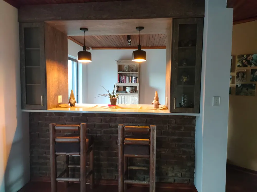 A serving hatch cut between two rooms, framed in dark woodgrain board with glass-fronted cabinets either side and pendant lights over the counter.