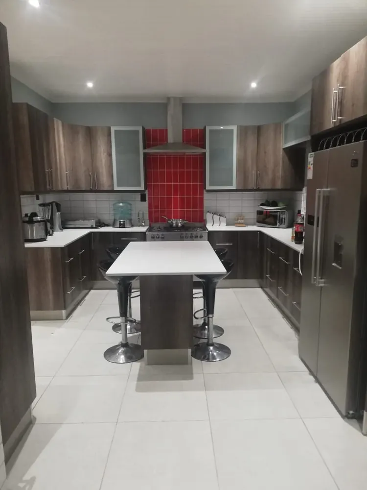 A dark oak kitchen seen end-on, with a central island and stools, frosted glass upper doors and a red tiled splashback.