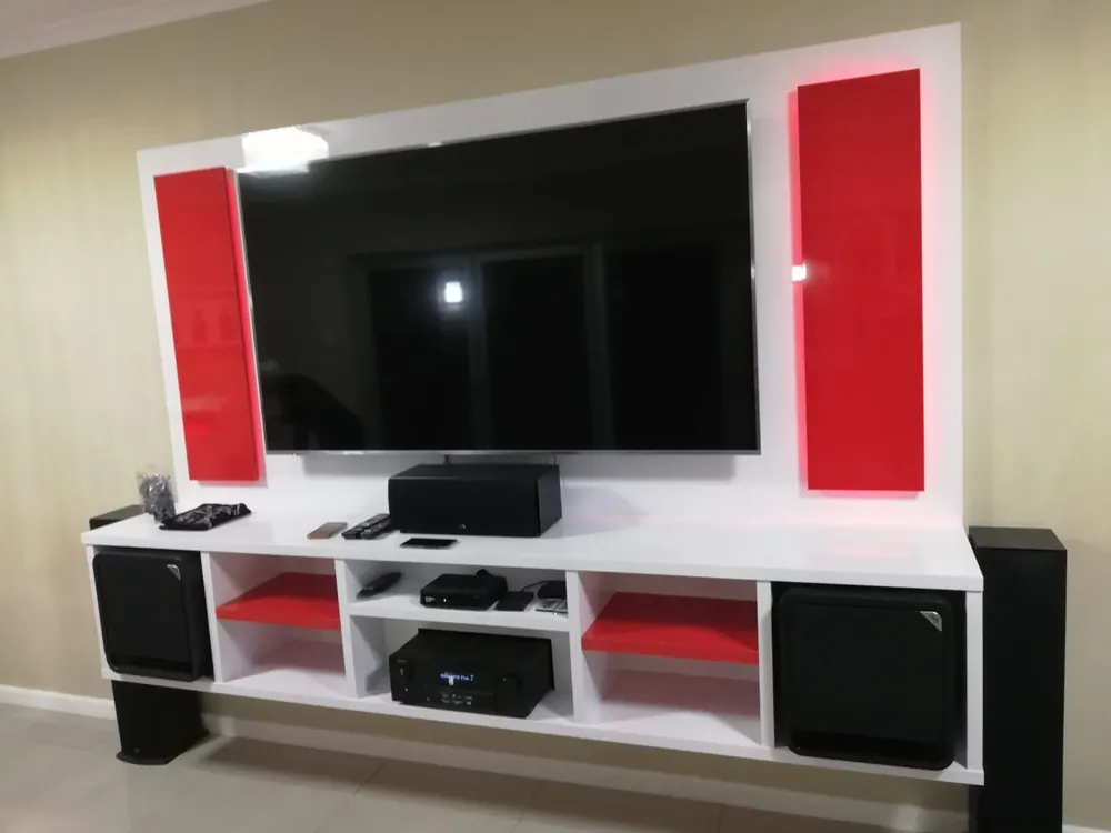 A floating white media unit with red gloss panels either side of a wall-mounted television and red shelves in the open compartments.