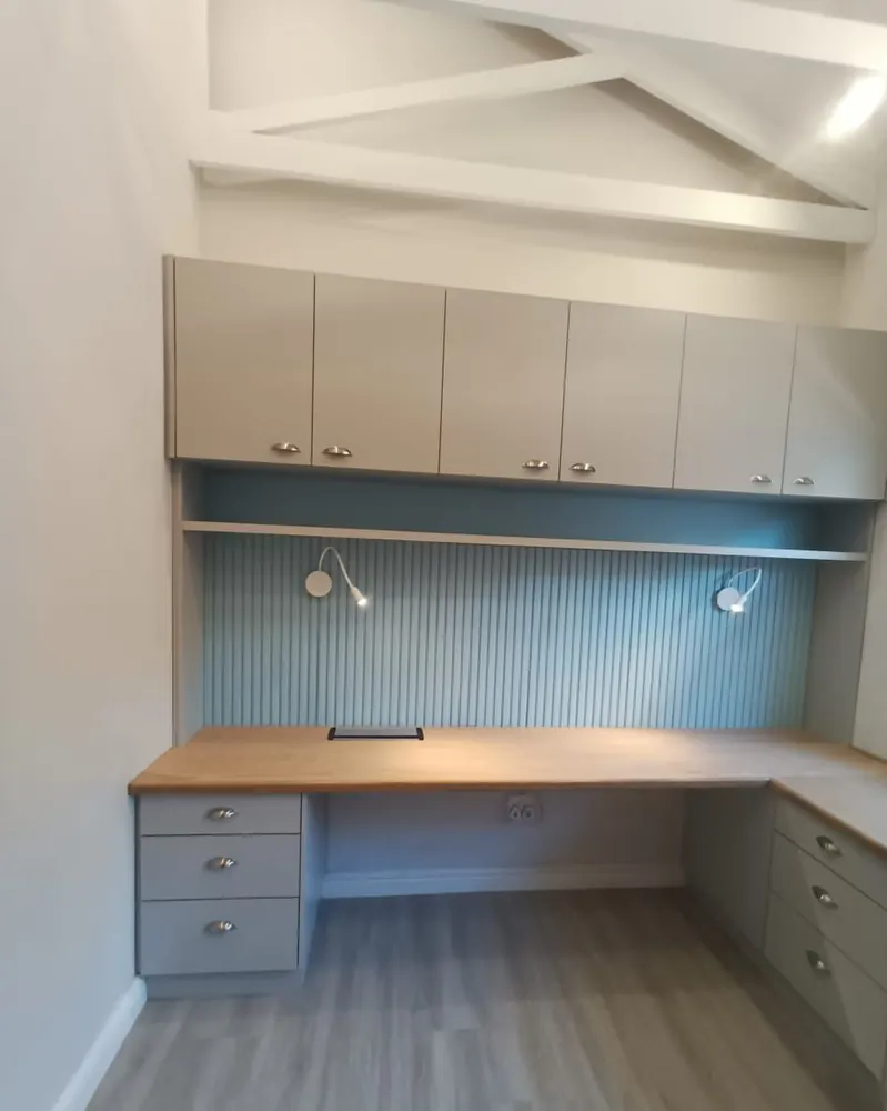 A wider view of the built-in study, showing the run of overhead cupboards, the oak desk returning along two walls and the fluted back panel.