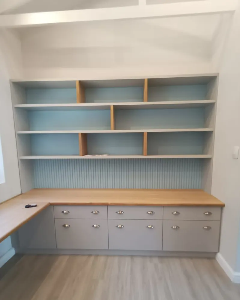 A built-in study with grey drawer units, a solid oak worktop, open shelves above and a pale blue fluted back panel.