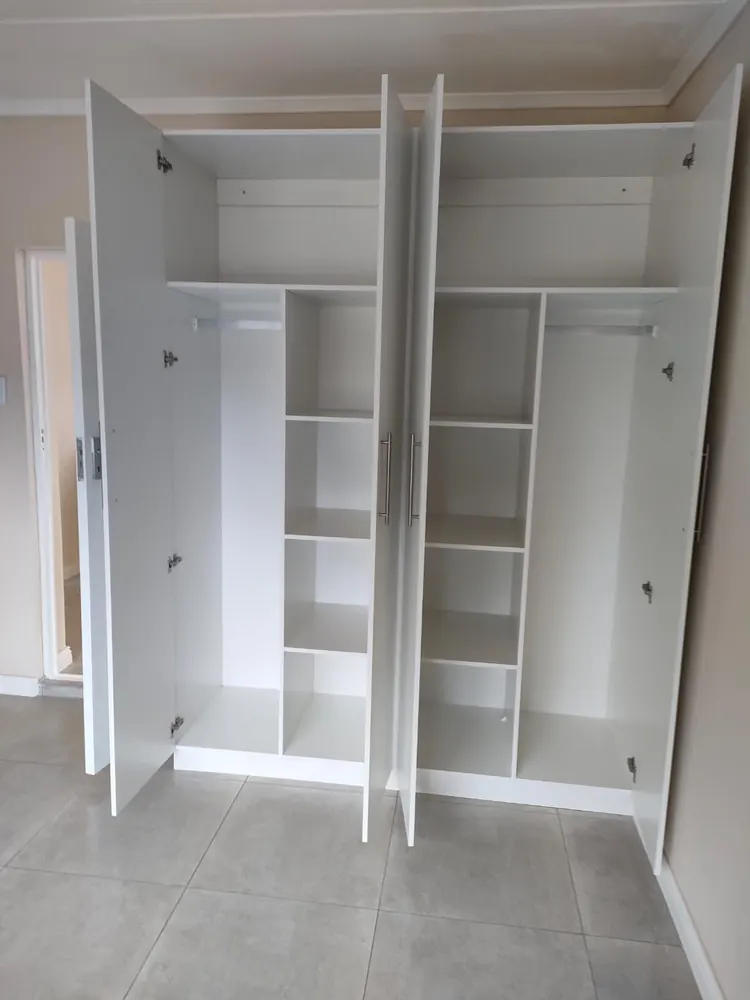 Two white built-in bedroom cupboards standing open, showing hanging rails, a bank of shelves down the centre and a full-height section either side.