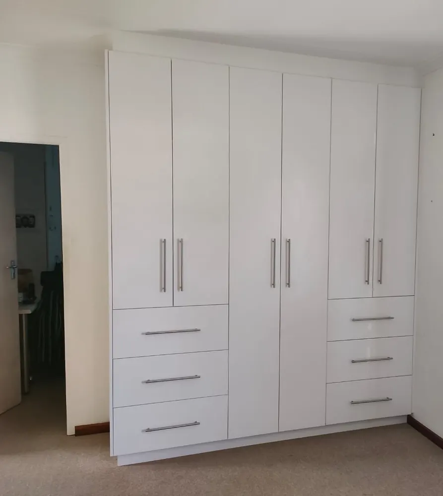 A wall of white built-in cupboards with long bar handles, tall doors above and three deep drawers on each side.